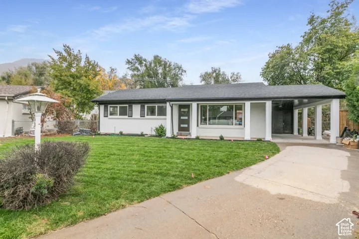 Single-story residence featuring white exterior masonry, a multi-column carport, a wide picture window, and a concrete driveway