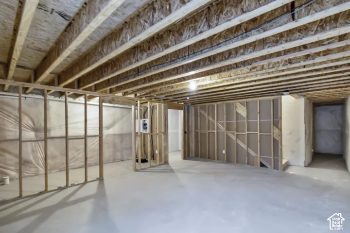 Unfinished interior space featuring exposed wood-stud framing, visible ceiling joists, concrete flooring, and vapor barrier wall protection