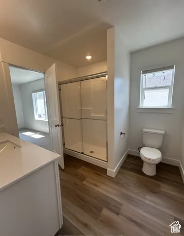 Bathroom featuring wood-finish flooring, a white vanity with a solid-surface countertop, a shower enclosure with sliding glass doors, and a porcelain toilet