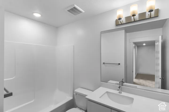 Bathroom featuring a composite tub surround, a vanity with a white countertop and integrated sink, a large wall-mounted mirror, and a three-light fixture