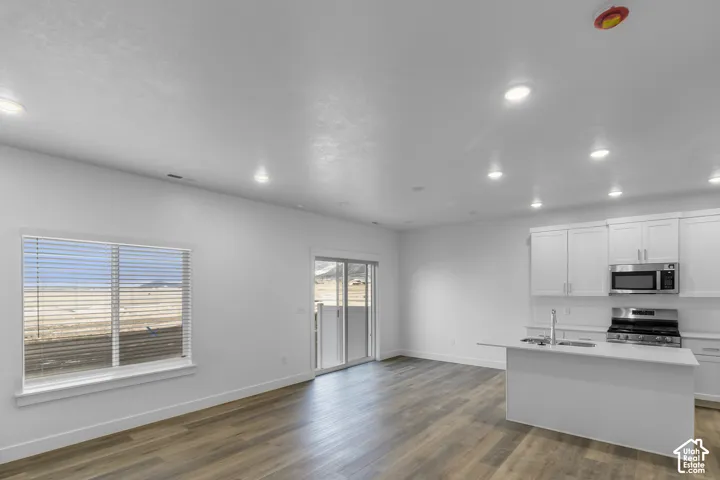 Open-concept interior featuring wood-finish flooring, white cabinetry, recessed lighting, stainless steel kitchen appliances, and sliding glass patio door