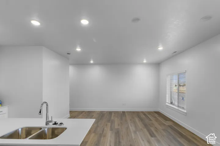 Kitchen island featuring a dual-basin stainless steel sink, gooseneck faucet, and white countertop, complemented by recessed lighting and wood-finish flooring