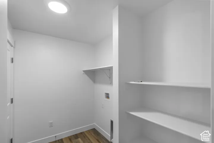 Utility space featuring wood-finish flooring, two tiers of built-in shelving, a dedicated recessed laundry hookup, and a flush-mount overhead light fixture