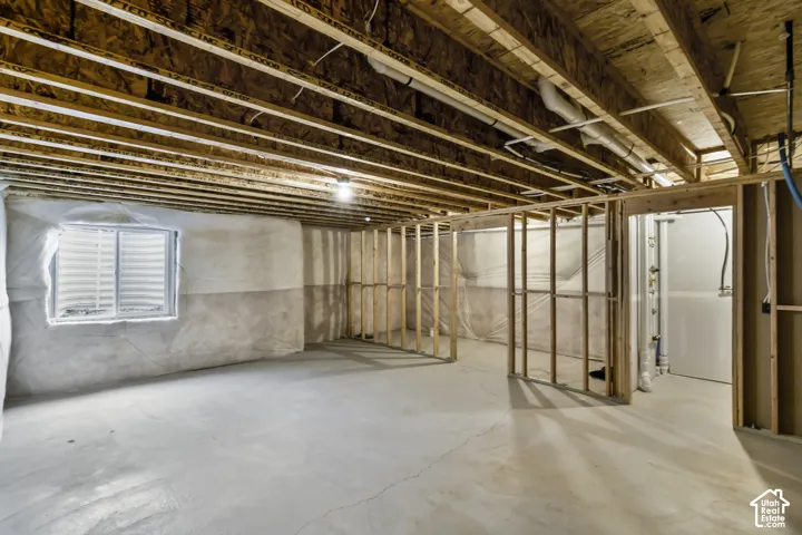 Unfinished lower level featuring exposed wood joist ceilings, concrete flooring, window with egress well, and wood-frame wall partitions