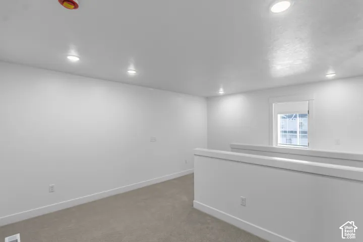 Neutral-toned wall-to-wall carpeting, recessed ceiling lighting, and a single window with white casing