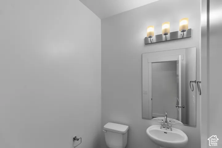 Powder room featuring a pedestal sink, wall-mounted three-light fixture with cylindrical glass shades, and a framed rectangular mirror
