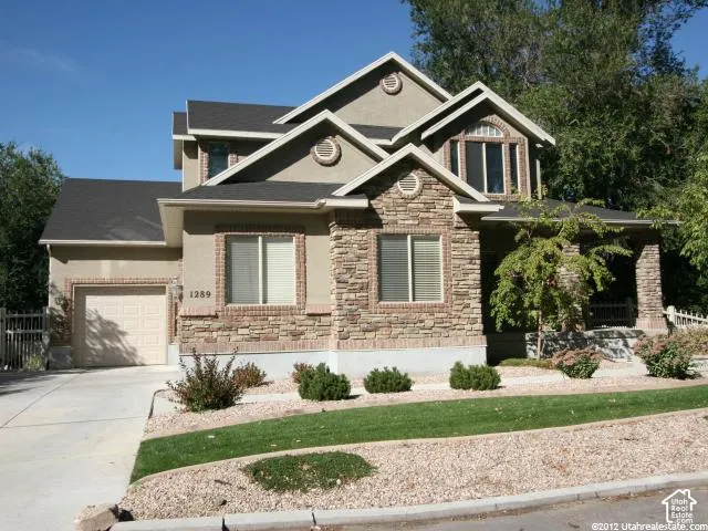 Multi-gabled exterior featuring stone veneer accents, stucco siding, a covered front porch with stone columns, and a concrete driveway