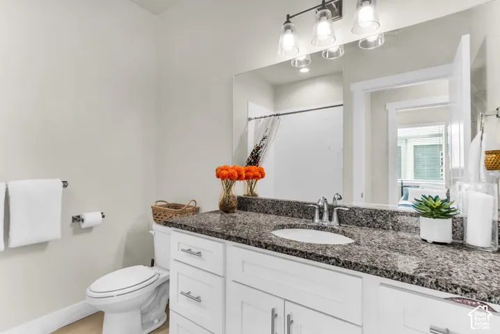 Bathroom featuring white cabinetry, stone-finish countertop with an integrated oval sink, three-light fixture, and large wall-mounted mirror