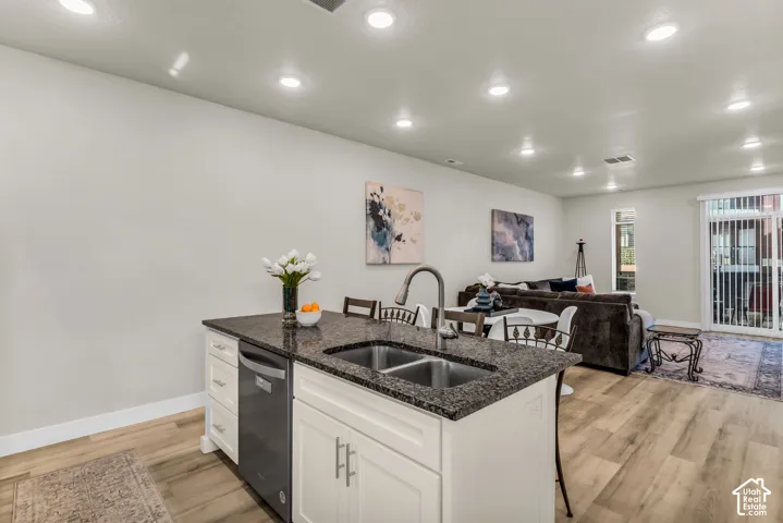 Kitchen island featuring white shaker-style cabinetry, dark stone-finish countertops, stainless steel dual-basin undermount sink, and integrated stainless steel dishwasher
