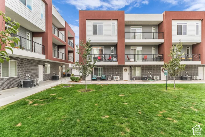 Multi-story exterior featuring a mix of horizontal siding, brick masonry, and smooth stucco finish, with integrated metal-railing balconies and concrete pathways