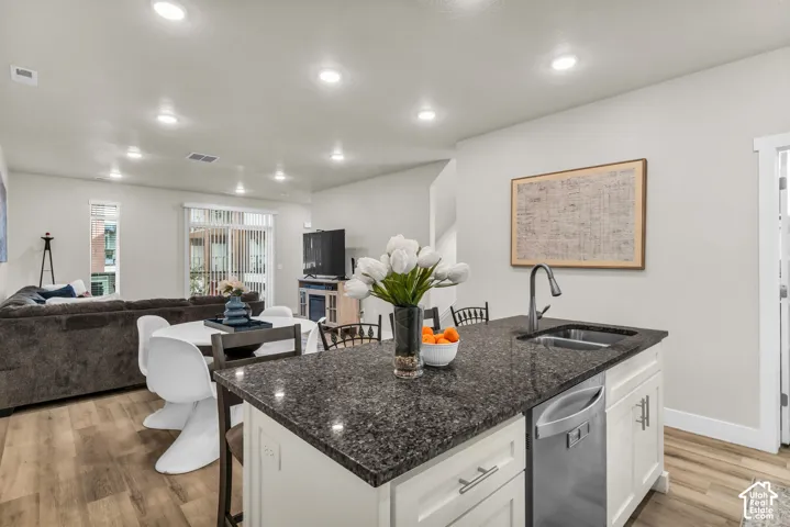 Kitchen island featuring a stone countertop, an integrated stainless steel dual-basin sink, high-arc faucet, white shaker-style cabinetry, and wood-finish flooring