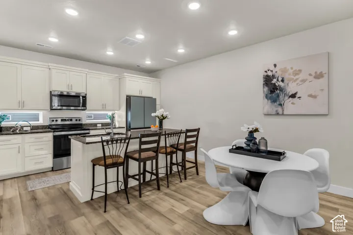 Kitchen featuring white cabinetry, dark countertops, a center island with bar seating, stainless steel appliances, and wood-finish flooring