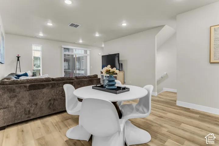 Open-concept living space featuring wood-finish flooring, recessed lighting, and vertical blinds on the sliding glass door