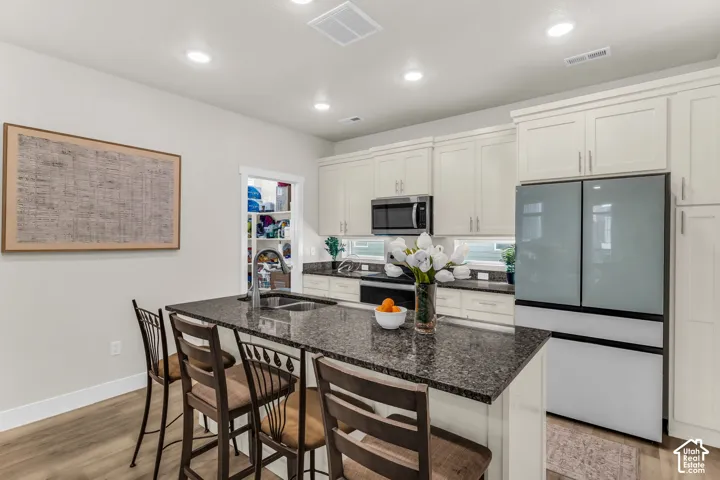Kitchen featuring shaker-style cabinetry, dark stone-finish countertops, recessed lighting, wood-finish flooring, and a central island with an undermount sink