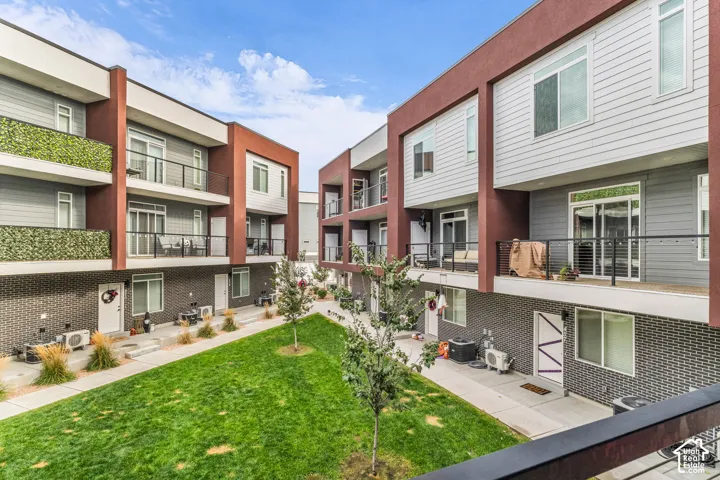 Contemporary multi-story exterior featuring dark brick masonry, horizontal siding, private balconies with black metal railings, and a central landscaped courtyard with turf and trees