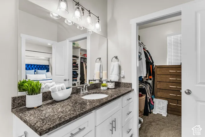 White cabinetry with brushed nickel hardware, expansive countertop, large wall-mounted mirror, multi-bulb vanity light fixture, and walk-in closet