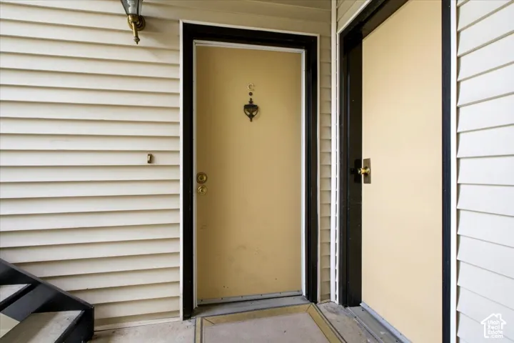 Exterior entry featuring horizontal siding, dark-trimmed door frames, brass-finish hardware, and wall-mounted exterior lighting