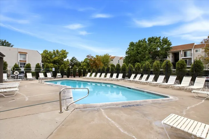 In-ground swimming pool featuring a concrete surround, metal perimeter fencing, and mature evergreen landscaping