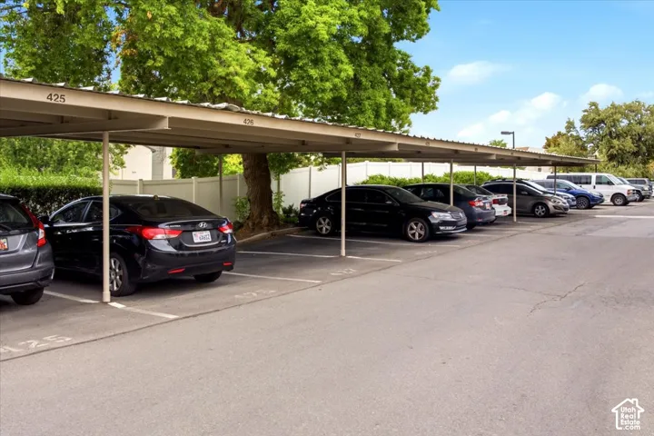 Covered parking structure featuring numbered stalls, asphalt paving, and white vinyl privacy fencing
