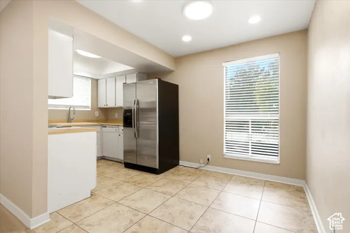 Kitchen area featuring tile flooring, white cabinetry, a stainless steel side-by-side refrigerator, recessed lighting, and a large window with horizontal blinds