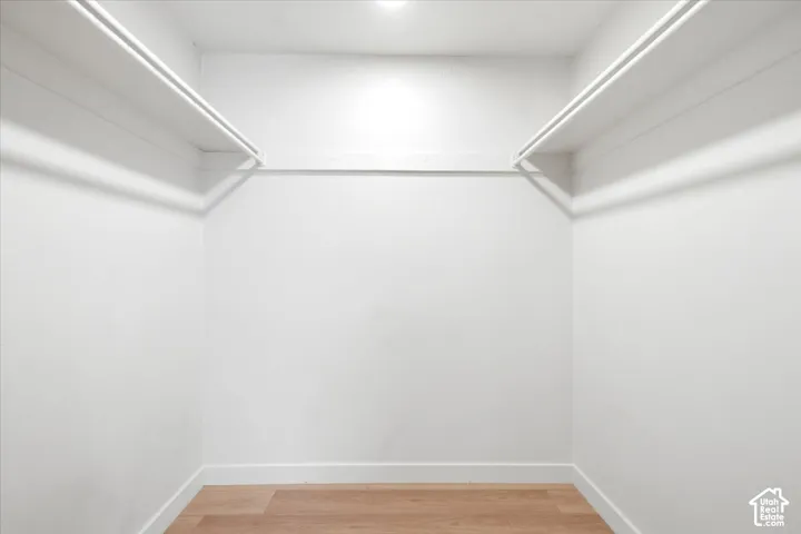 Walk-in closet featuring wood-finish flooring, dual-level white shelving, and white walls
