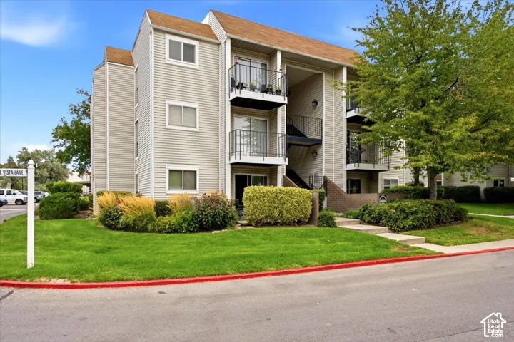 Three-story multi-family exterior featuring light-toned horizontal siding, dark metal balcony railings, and gable roofing