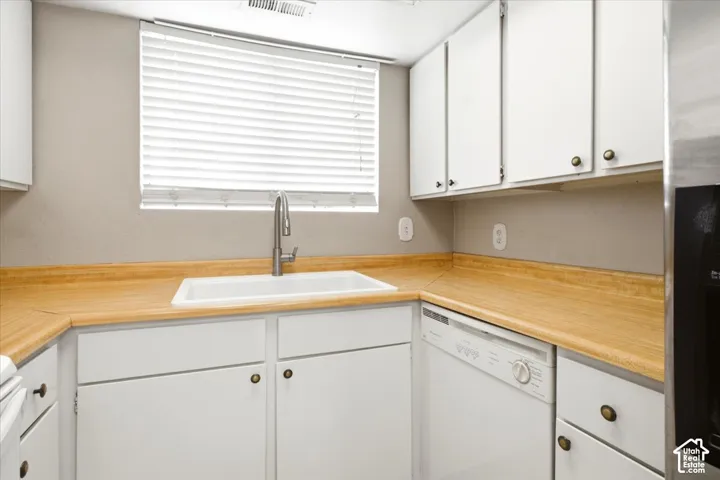 Kitchen featuring white cabinetry, light-toned laminate countertops, a white undermount sink with a gooseneck faucet, and an integrated white dishwasher