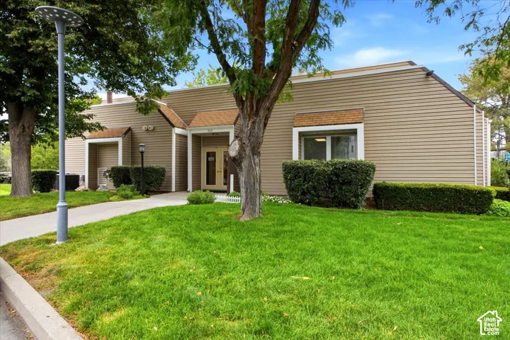 Exterior featuring horizontal siding, recessed entry, shingled accent gables, concrete walkway, and landscaped lawn with mature trees