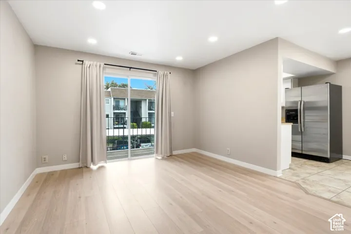 Wood-finish flooring, recessed lighting, sliding glass door to exterior balcony, and stainless steel refrigerator