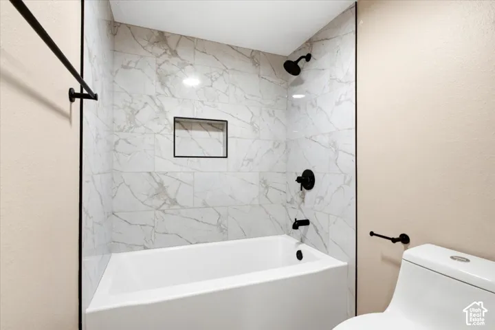Full-height tub surround featuring large-format veined tile, integrated recessed shelving, and matte black plumbing fixtures