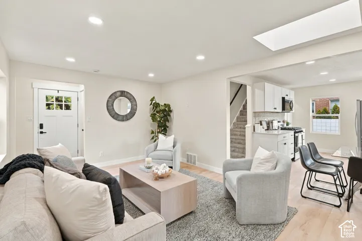 Open-concept interior featuring light wood-finish flooring, recessed lighting, a ceiling skylight, and white cabinetry