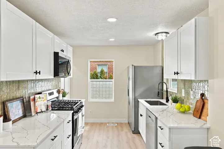 Kitchen featuring white shaker-style cabinetry, white countertops with grey veining, integrated stainless steel appliances, textured tile backsplash, and wood-finish flooring