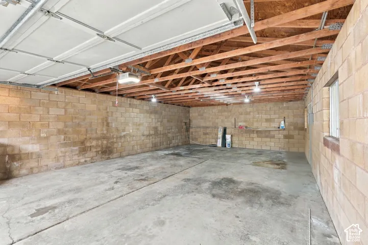 Garage interior featuring exposed wood-truss ceiling, concrete flooring, and concrete block walls