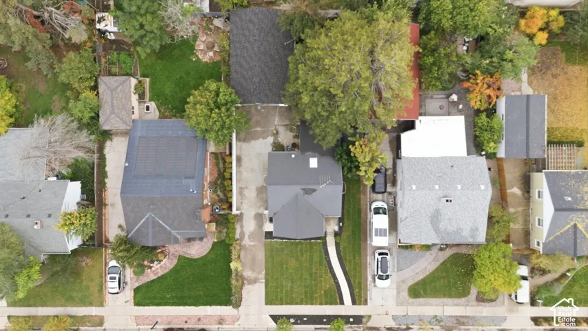 Aerial perspective featuring a manicured front lawn, paved driveway, dedicated walkway, and mature trees