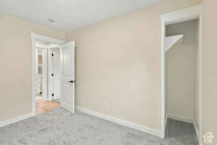 Neutral-toned room featuring grey wall-to-wall carpeting, white interior doors with dark hardware, minimalist white trim, and a built-in closet with integrated shelving