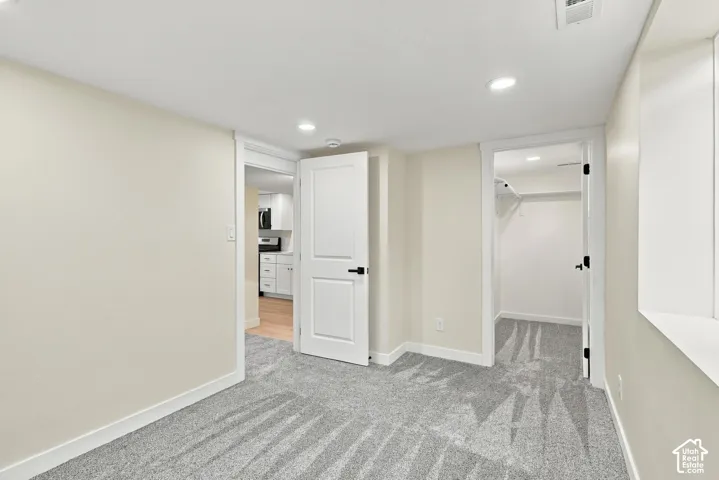 Neutral-toned interior space featuring wall-to-wall carpeting, recessed ceiling lighting, a two-panel interior door with matte black hardware, and an open-door closet with built-in shelving