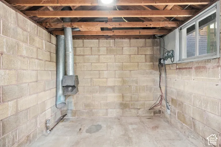 Unfinished storage area featuring exposed wood ceiling joists, concrete block walls, a sliding window, and concrete flooring
