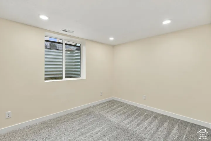 Interior room featuring neutral wall paint, recessed lighting, carpeted flooring, and an egress window with a corrugated metal window well