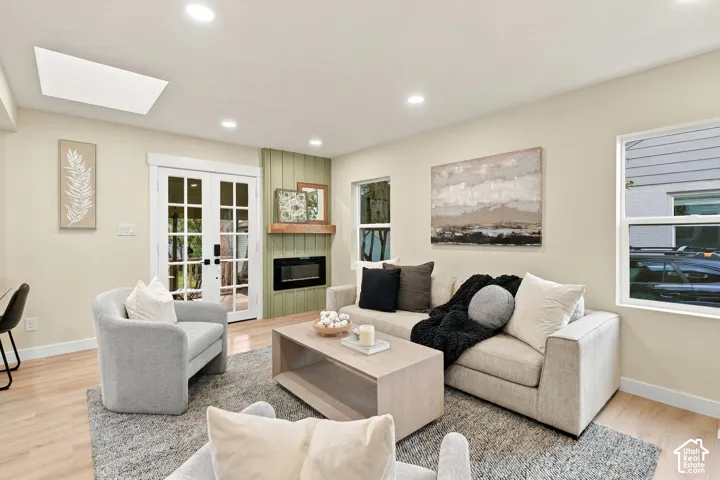 Recessed lighting, wood-finish flooring, skylight, wall-mounted electric fireplace with a wood mantel, and French glass doors