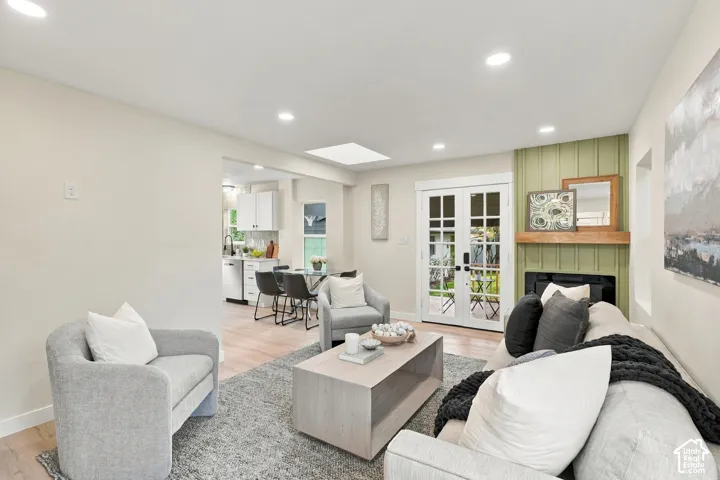 Living space featuring recessed lighting, a skylight, wood-finish flooring, glass-paned French doors, and a fireplace with vertical paneled accent wall and wood mantel