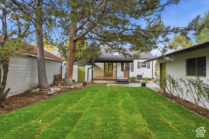 Backyard featuring a manicured lawn, elevated wood deck with railing, mature trees, and concrete hardscaping