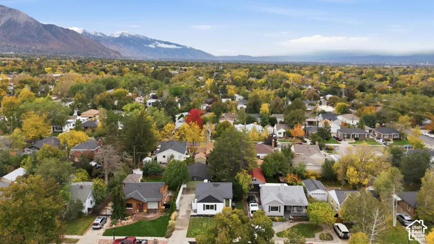 Aerial perspective of the residential property featuring mature trees, landscaped lawns, and mountain backdrop
