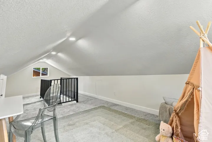 Vaulted ceiling with recessed lighting, wall-to-wall carpeting, and black metal stair railing
