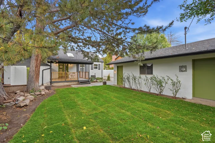 Backyard featuring a manicured lawn, elevated wood-decked patio, detached structure with painted brick exterior, and mature pine trees