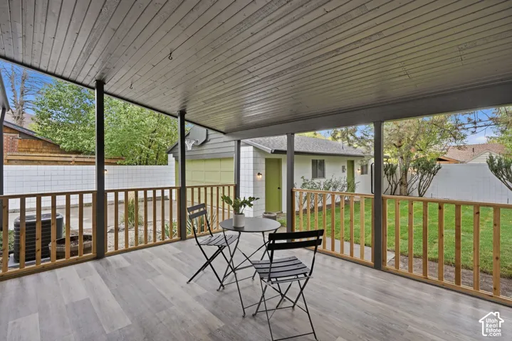 Covered patio featuring wood-finish flooring, metal support posts, and wooden railings overlooking a fenced backyard