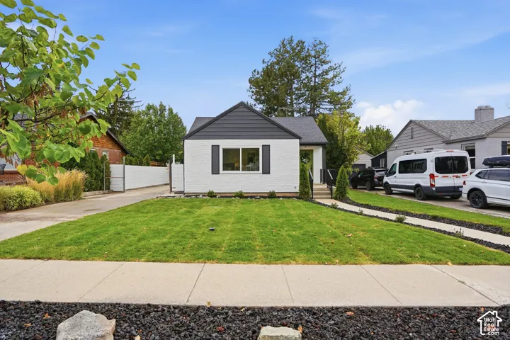 Exterior featuring white painted brick masonry, dark horizontal gable siding, decorative shutters, a concrete walkway, and a manicured lawn