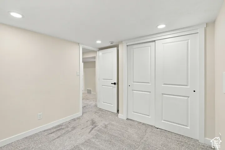 Interior space featuring recessed lighting, neutral wall paint, wall-to-wall carpeting, a double-door sliding closet, and a white interior door with matte black hardware
