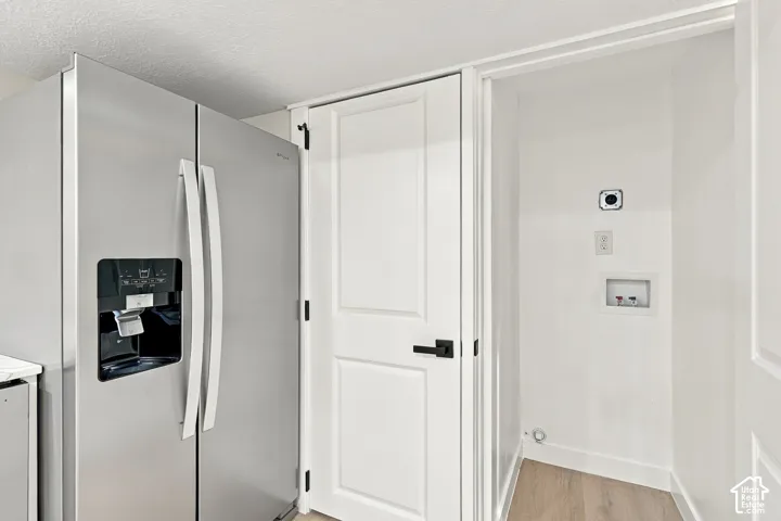Stainless steel side-by-side refrigerator, white interior door with matte black lever handle, wood-finish flooring, and recessed utility alcove with integrated water hookups