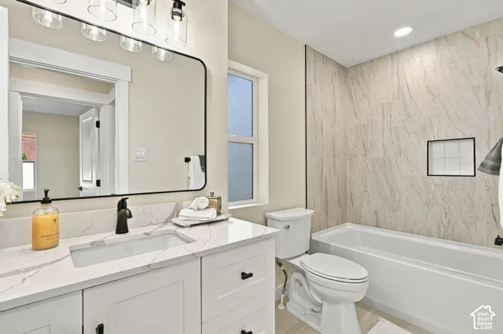 White vanity featuring a solid surface countertop with integrated sink and matte black faucet, wall-mounted mirror with black frame, four-light vanity fixture, and bathtub surround with large-format wall tile and built-in recessed niche