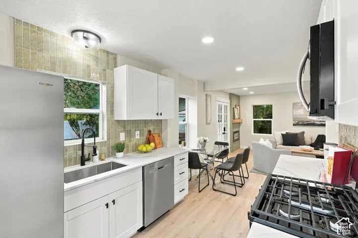 Kitchen featuring white shaker-style cabinetry, stone-patterned countertops, textured vertical tile backsplash, stainless steel appliances, and wood-finish flooring